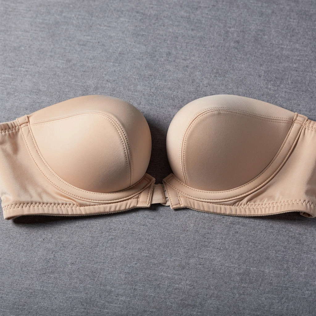 Plunge z ekstremalnie niskim mostkiem w odcieniu beżu położony na szarej fakturalnej powierzchni. Widoczne wyraźnie wyprofilowanie miseczek i szerokie boczne usztywnienie. Kadr z boku, padające światło podkreślające zagłębienie centralne, ostre detale konstrukcyjne.